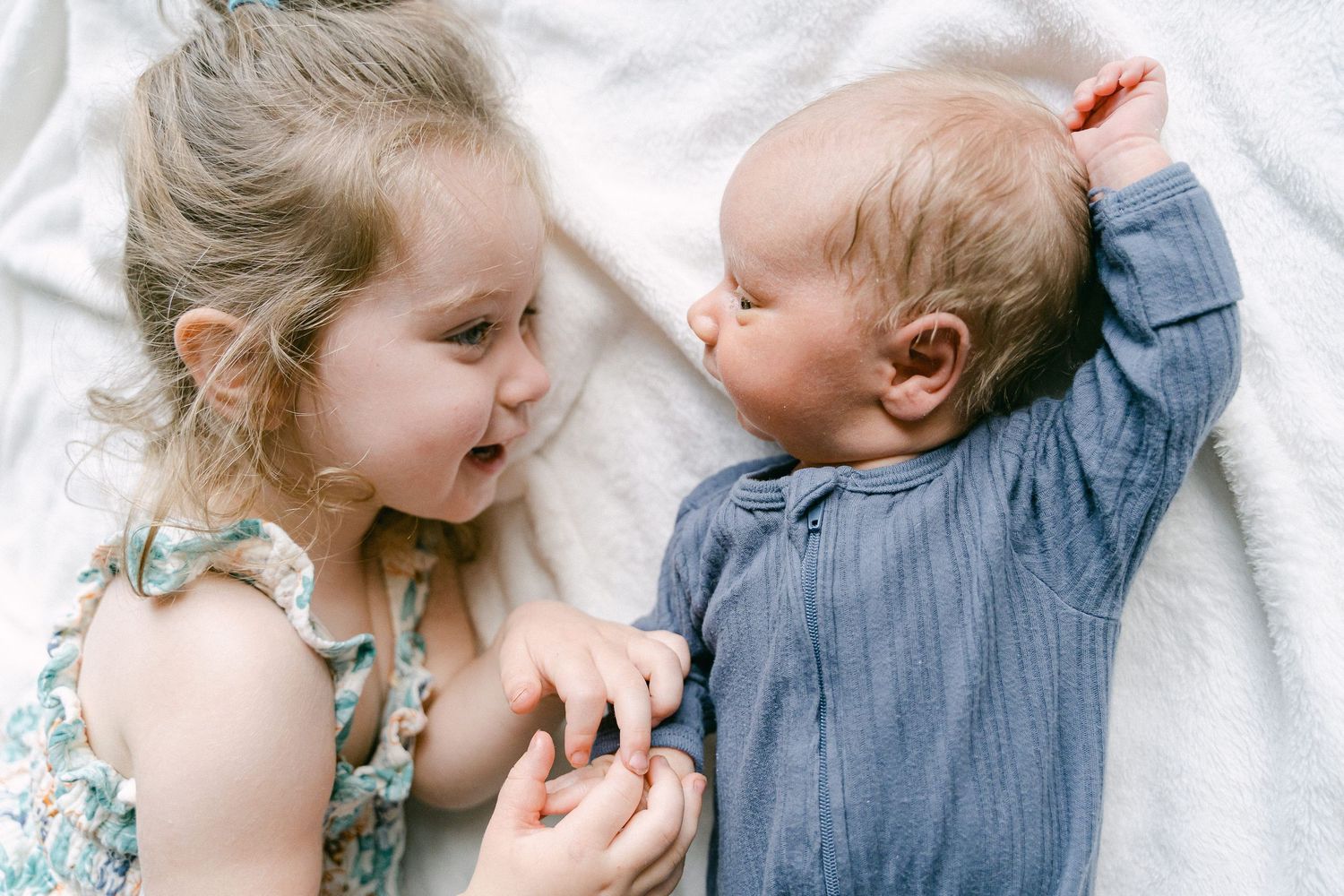 Two young children lying on white bedding share a sweet moment of laughter and connection.