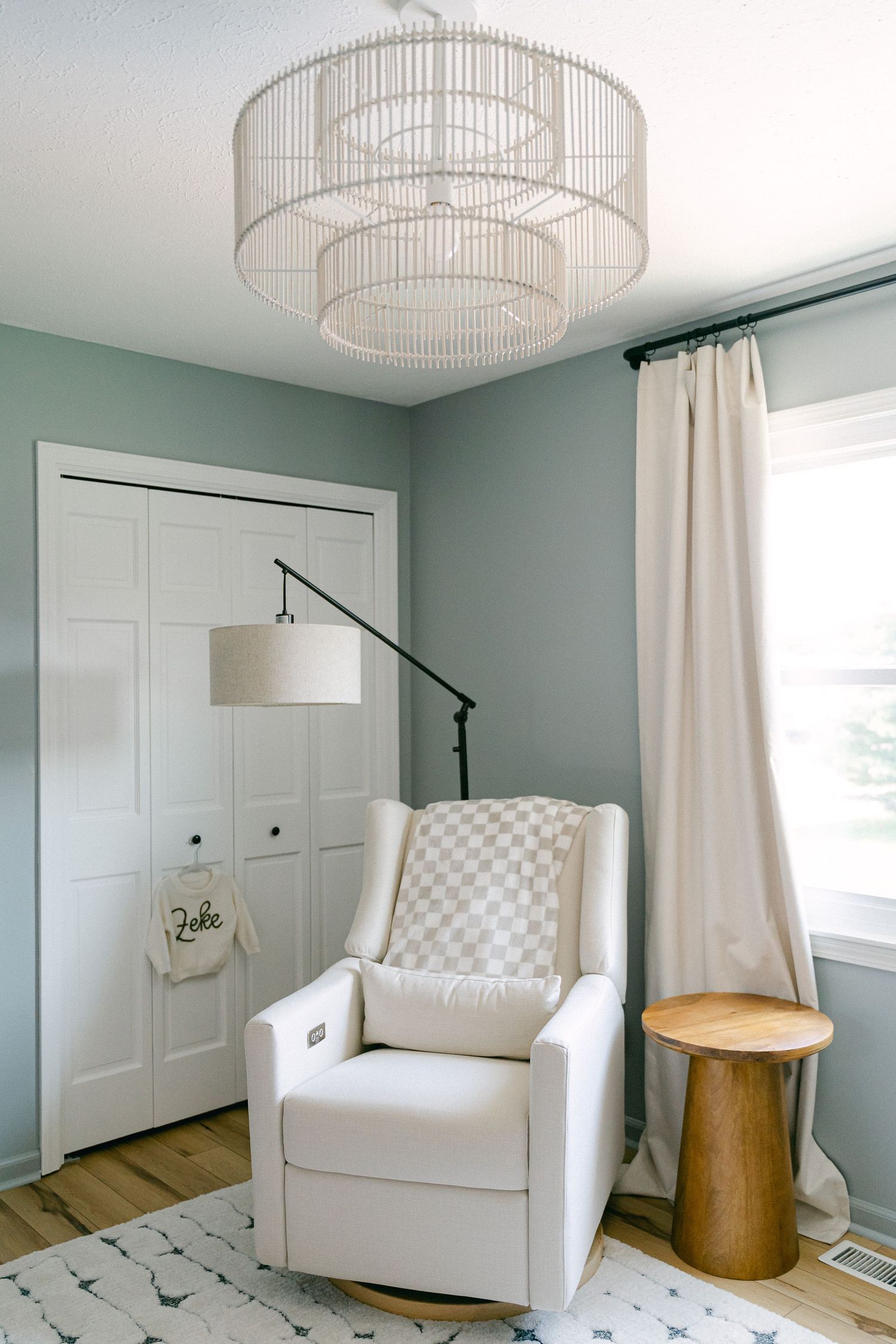 Modern nursery room features a white tufted armchair, wooden side table and elegant drum pendant light fixture.