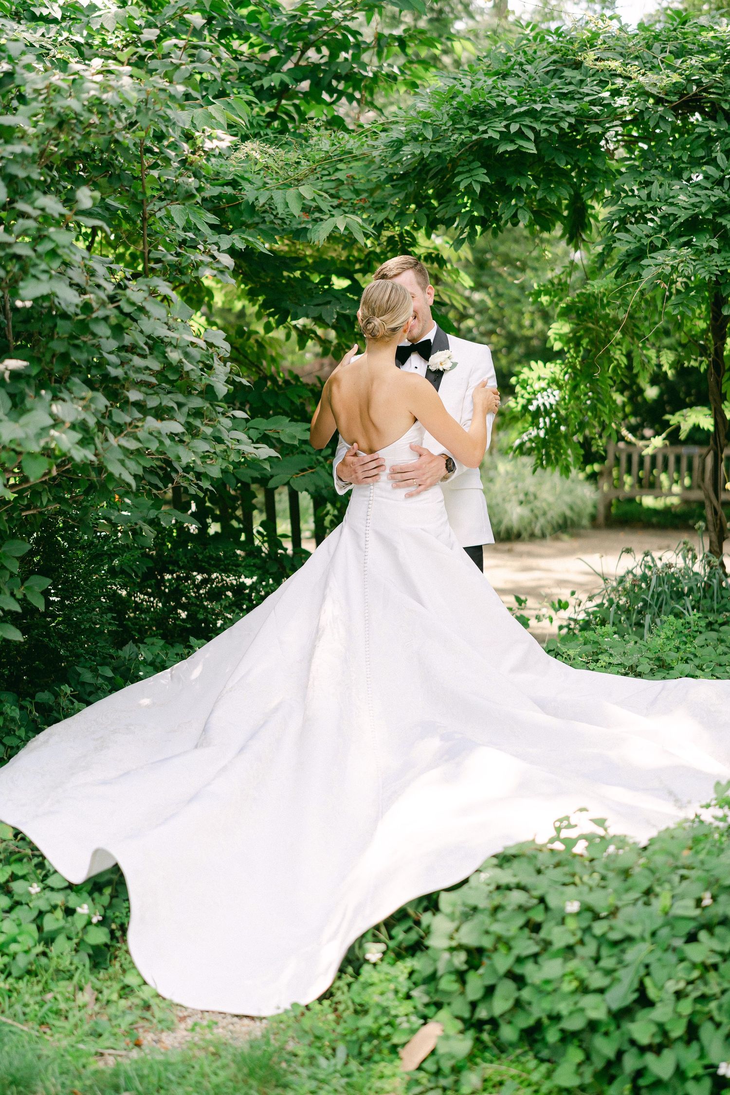 Bride and groom embrace in lush garden, her white gown with long train flowing elegantly as he holds her close in South Bend, IN