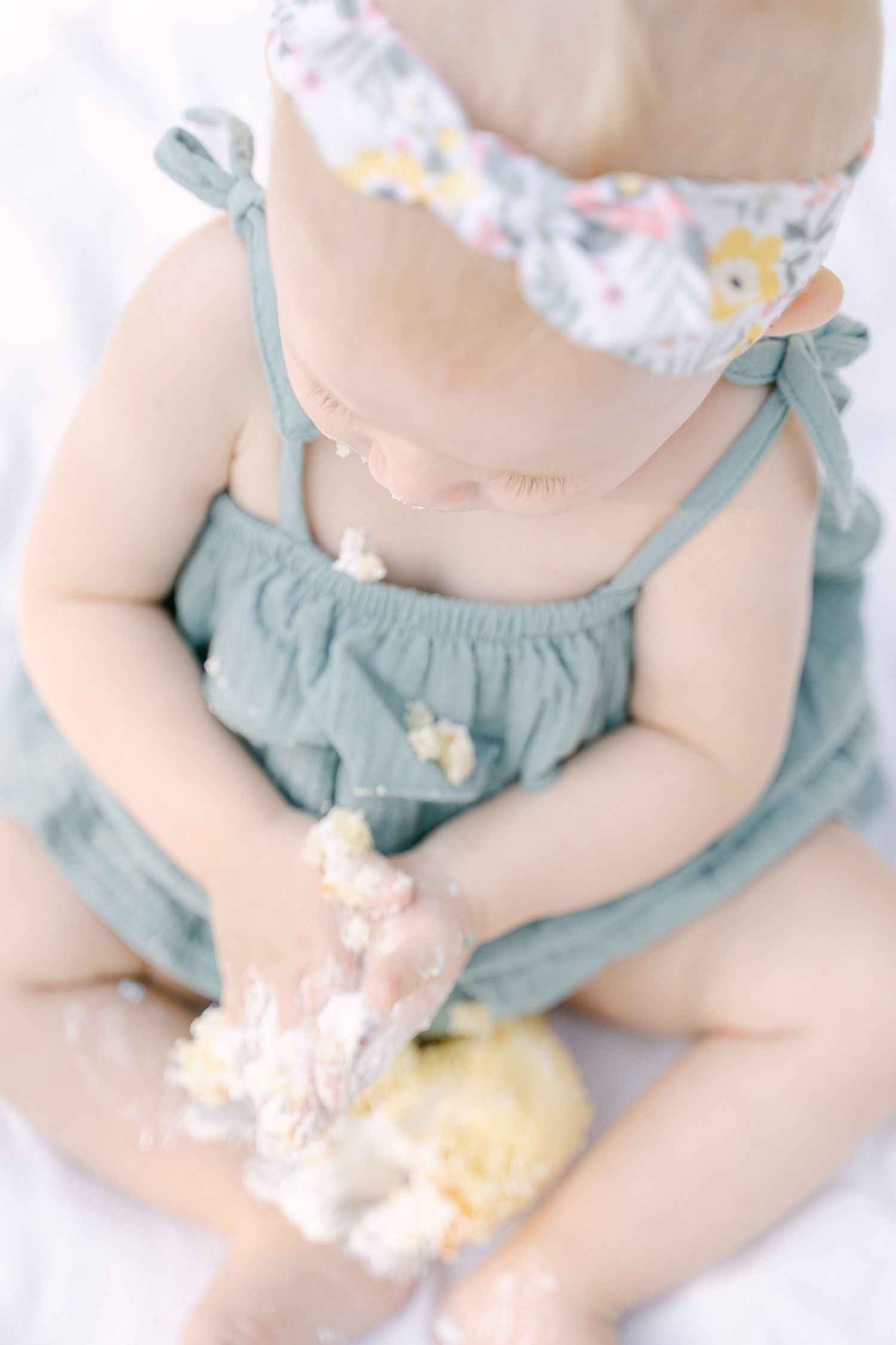 Close up of baby hands playing with cake or dessert while wearing blue outfit.