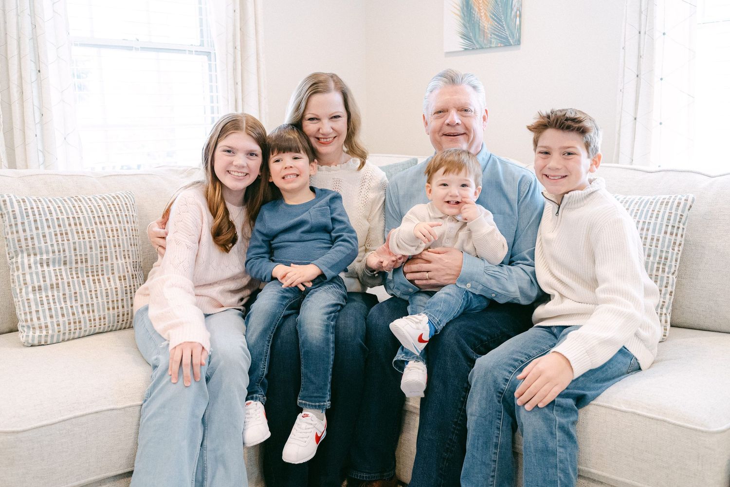 A family sits together on a couch in a bright living room wearing coordinated blue and white outfits.