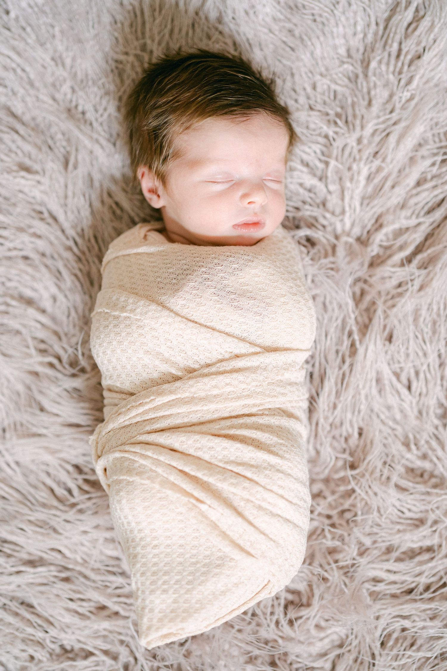 A progression of photos showing a sleeping newborn wrapped in cream-colored swaddle blanket on fluffy white fur.