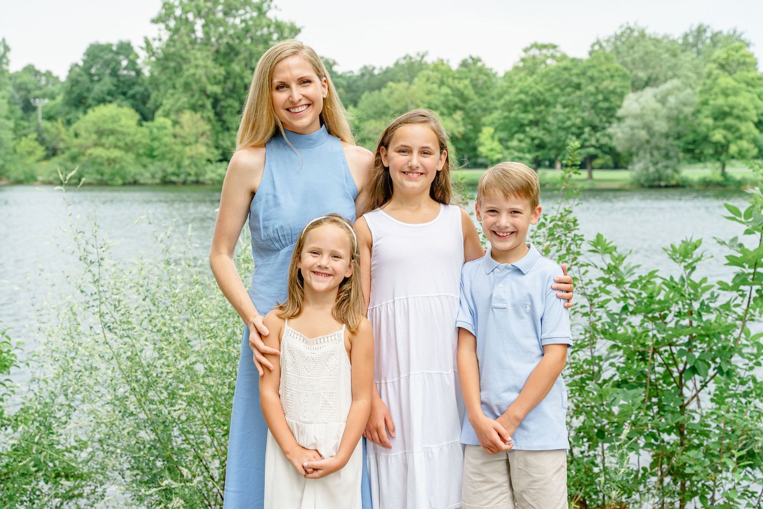 A small group stands together for a portrait by a scenic lake with natural foliage.