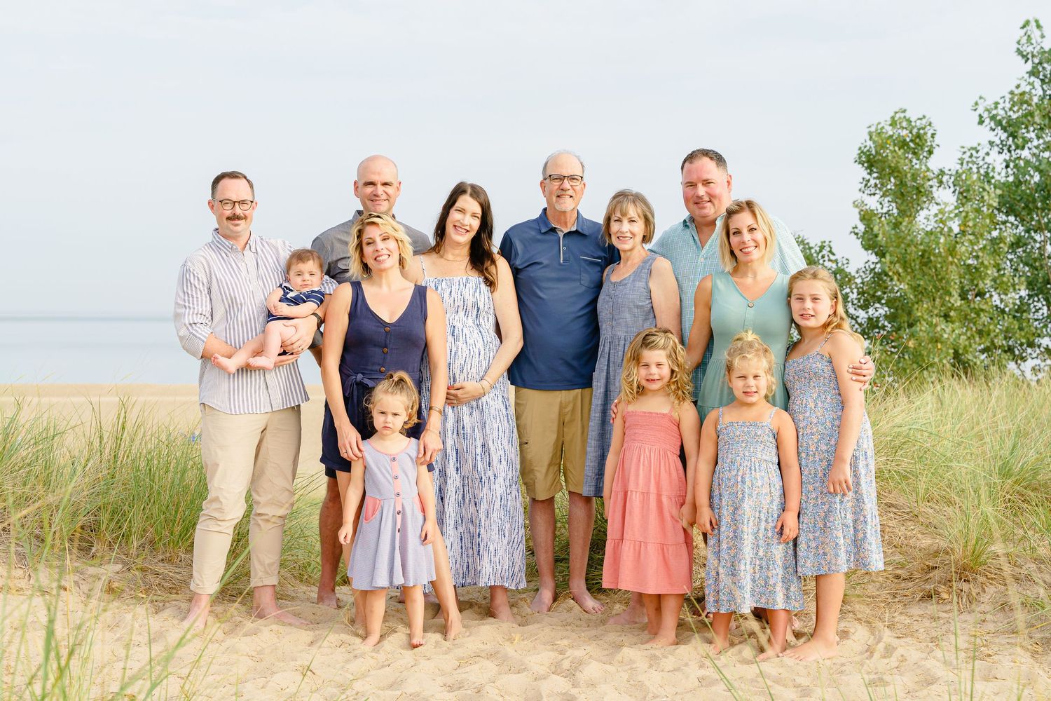 Family group wearing coordinated blue and coral outfits poses together on sandy beach path at sunset.