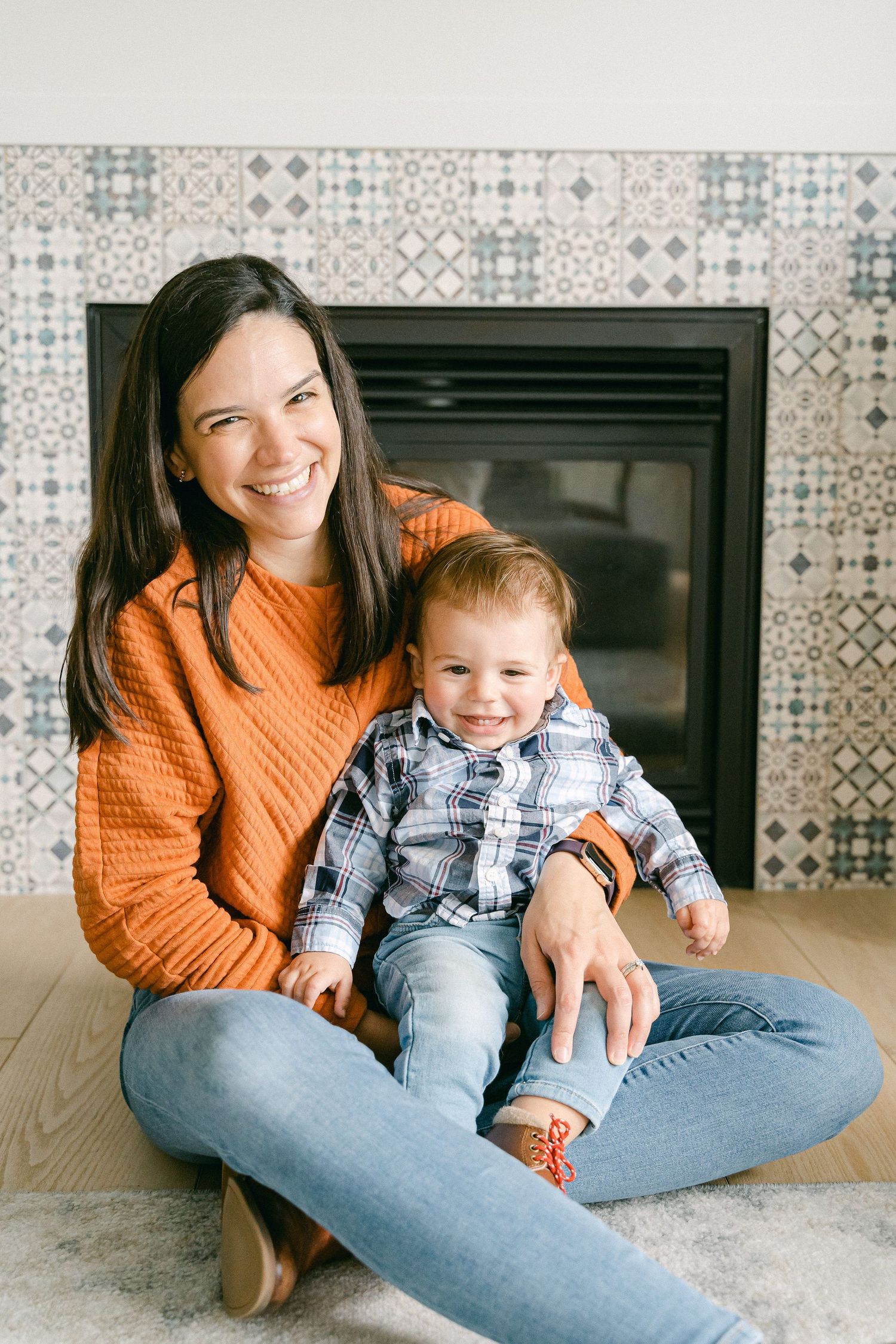 A parent and child sit together on the floor wearing orange and plaid, sharing playful moments in a modern room.
