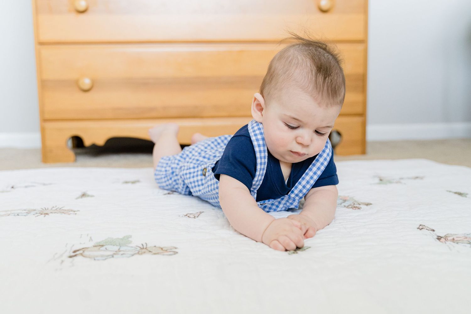 A toddler in a blue and white outfit plays with toys on a light colored carpet.