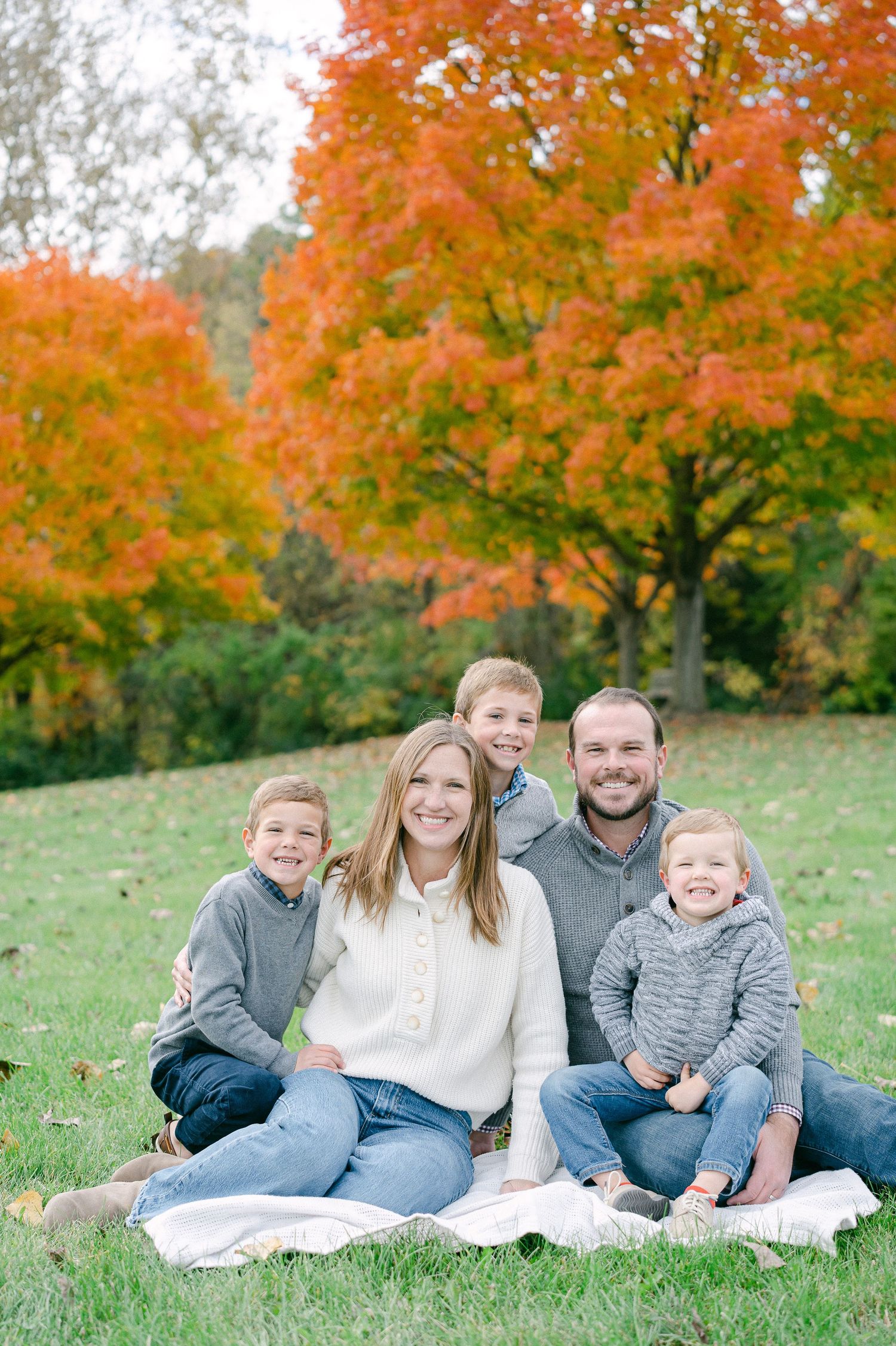 A family relaxes together on a white blanket against vibrant orange autumn foliage in the background.