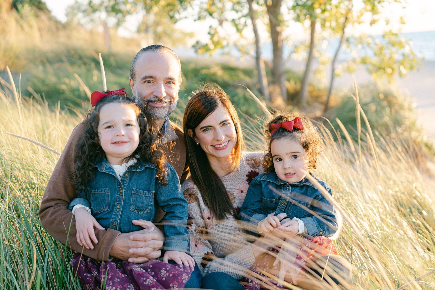 A family sits together in golden grass during a sunset photo session at a hillside park.