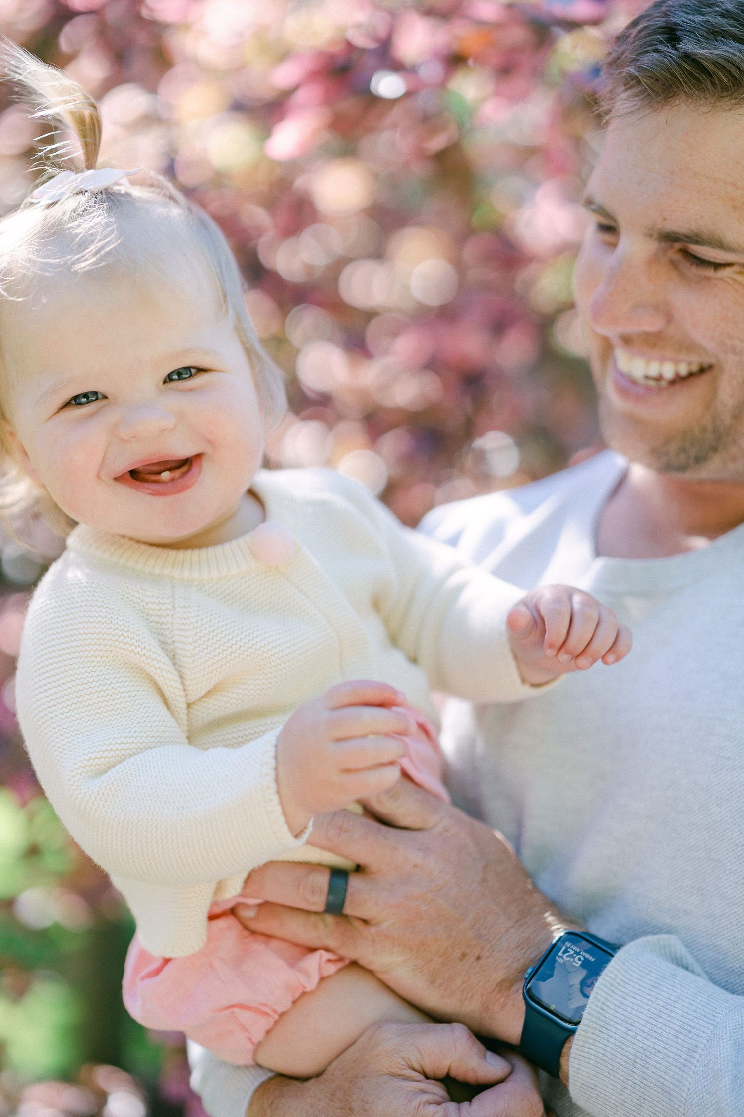A joyful outdoor family portrait with soft bokeh and pink blossoms in the background.