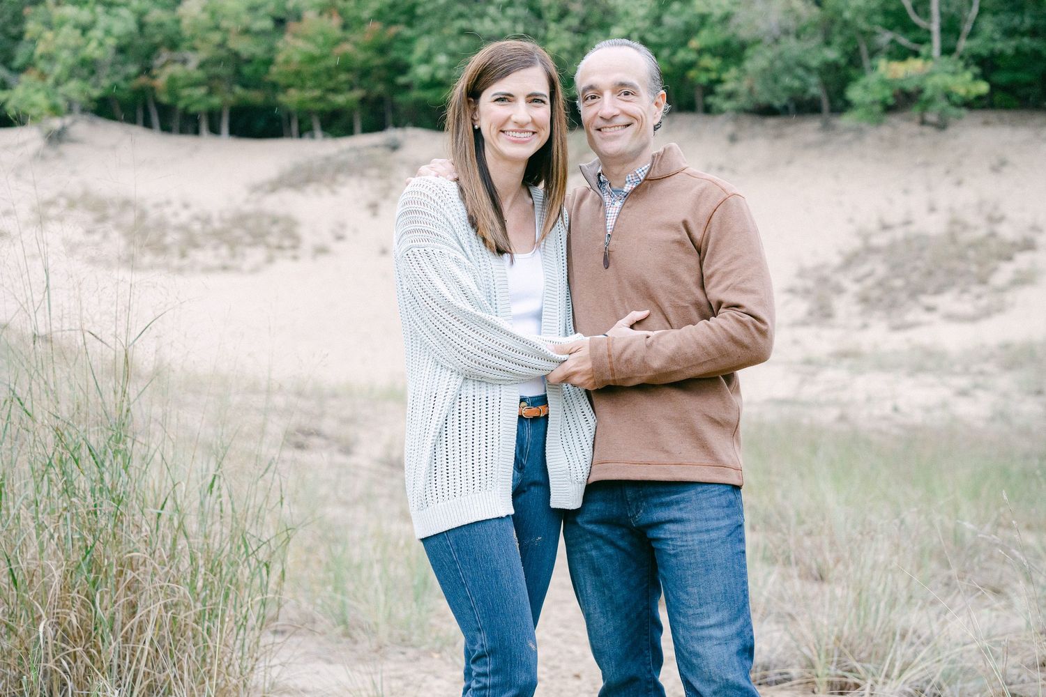 A couple shares affectionate moments together in an outdoor field with tall grass and natural lighting.