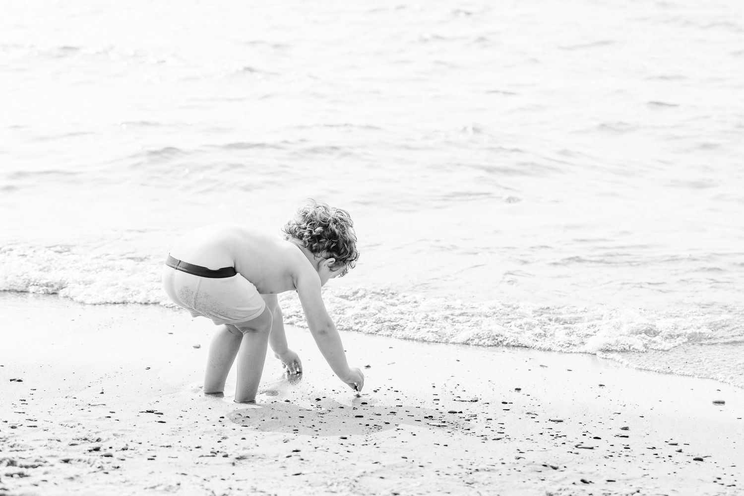 Black and white image of people collecting shells and exploring on a sandy beach.