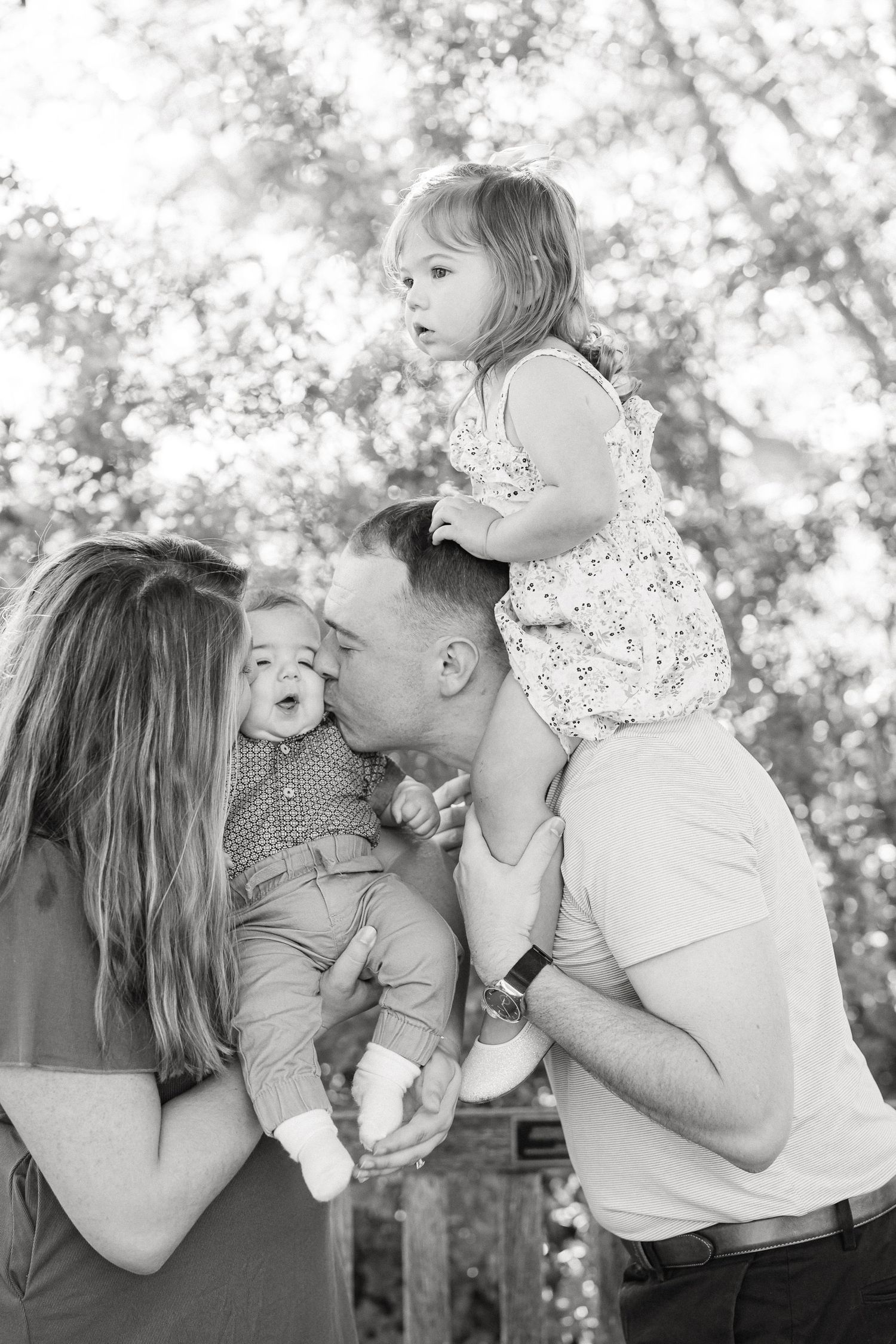 Black and white outdoor family portrait showing playful interaction and joyful expressions in a natural setting.