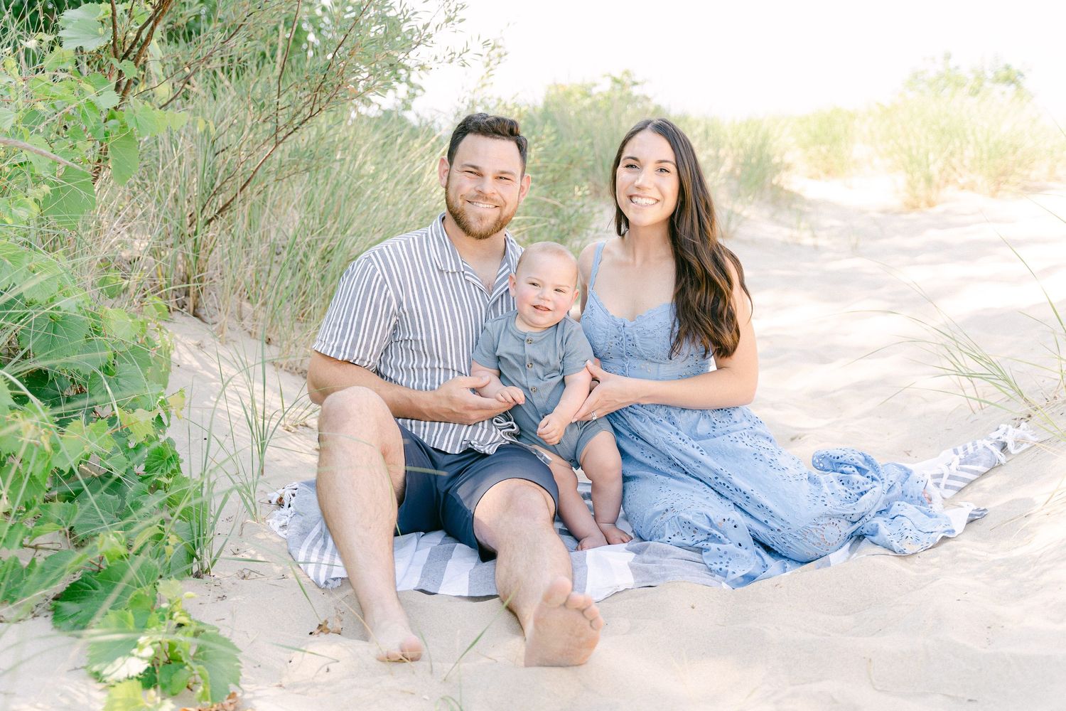 A family in light blue outfits sits together on a sandy beach path during a sunny outdoor photo session.
