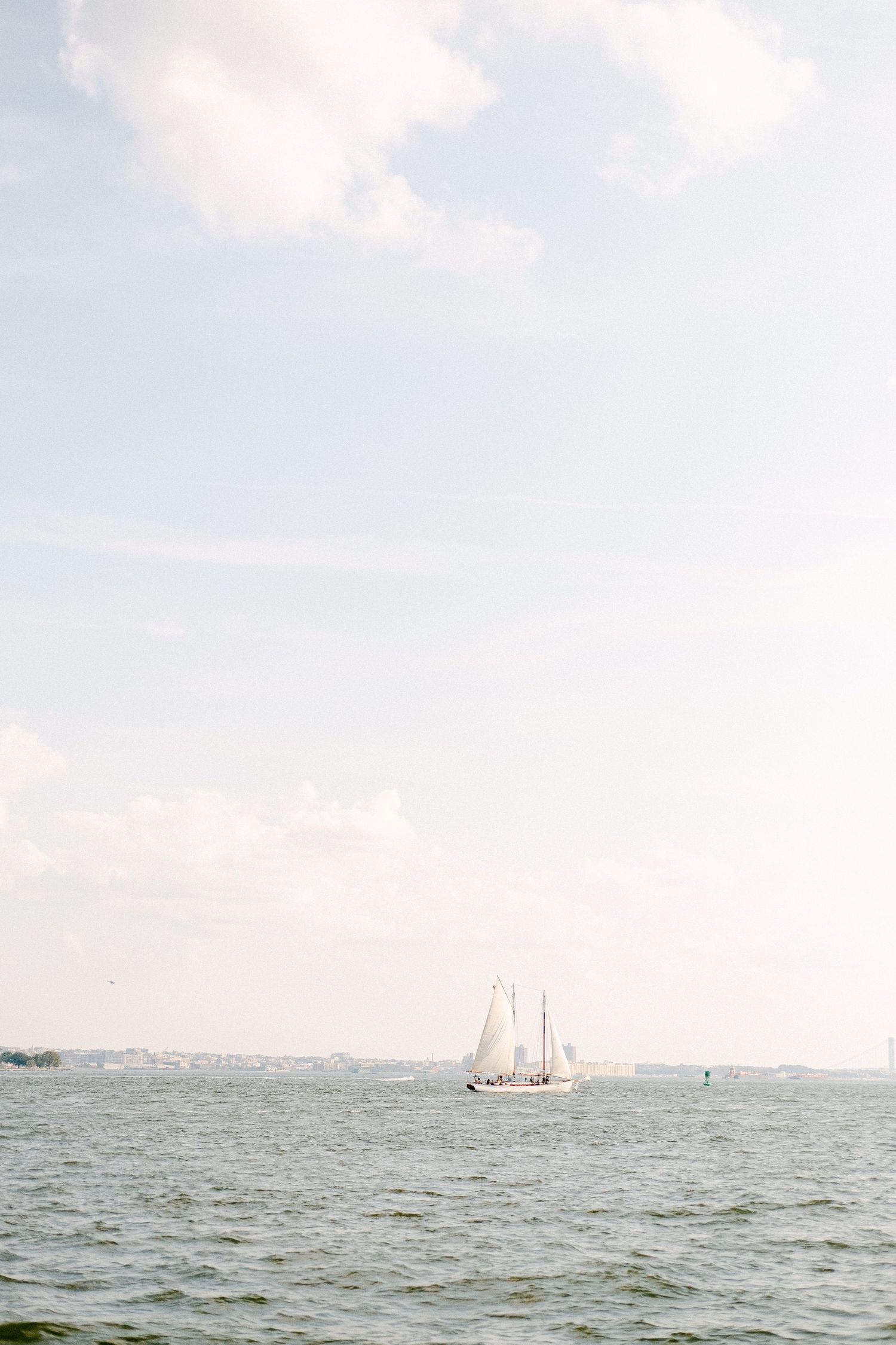 A serene seascape with a distant sailboat on the horizon under a soft, cloudy sky.
