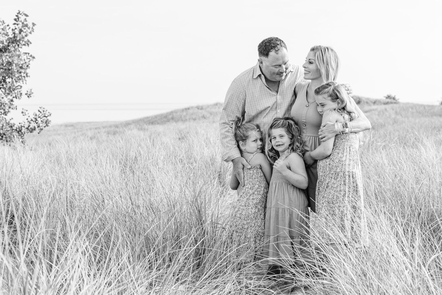A couple shares tender moments together in a sun-drenched field of tall grass captured in black and white photography.