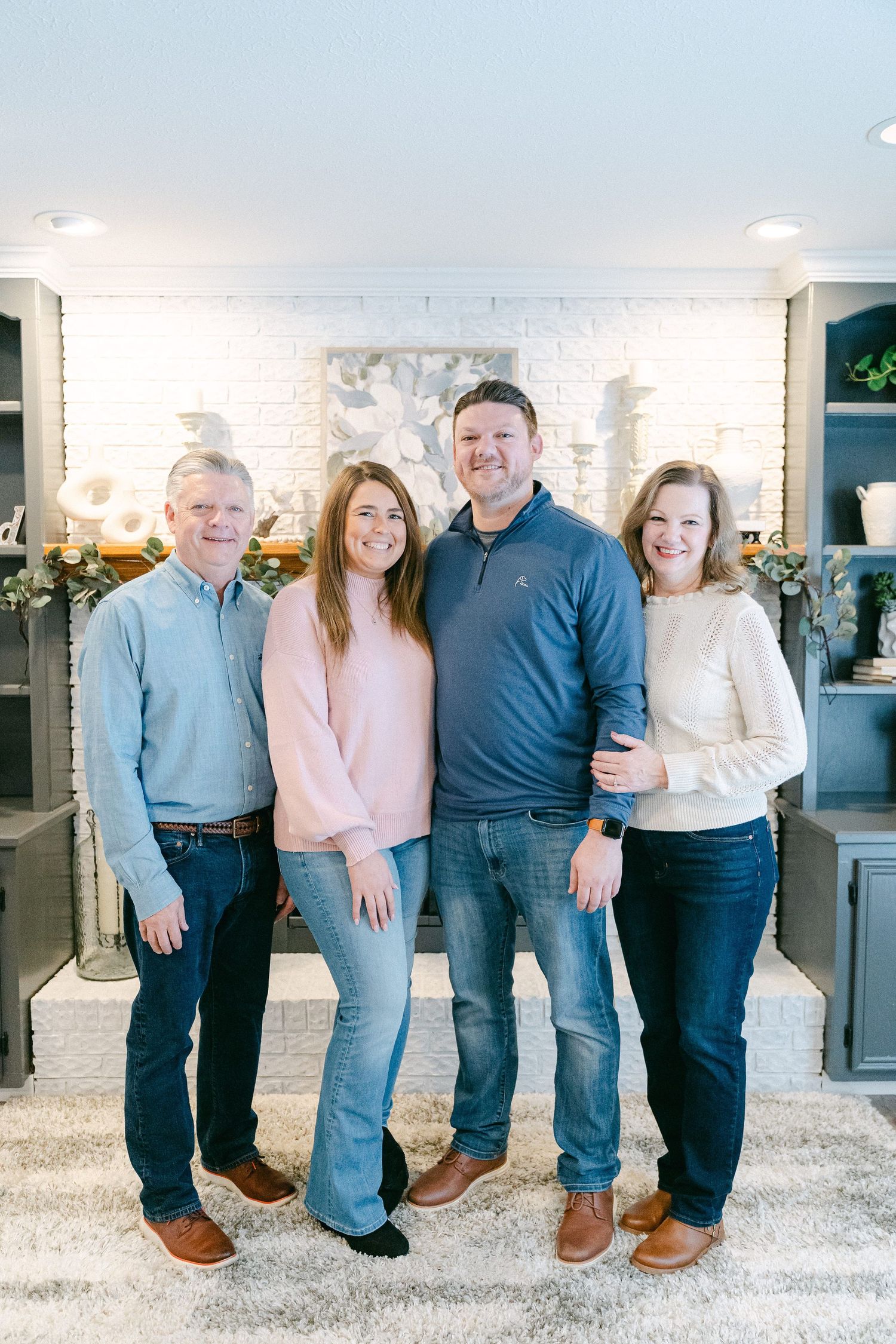 Family group poses together in coordinated casual outfits against a bright interior background.