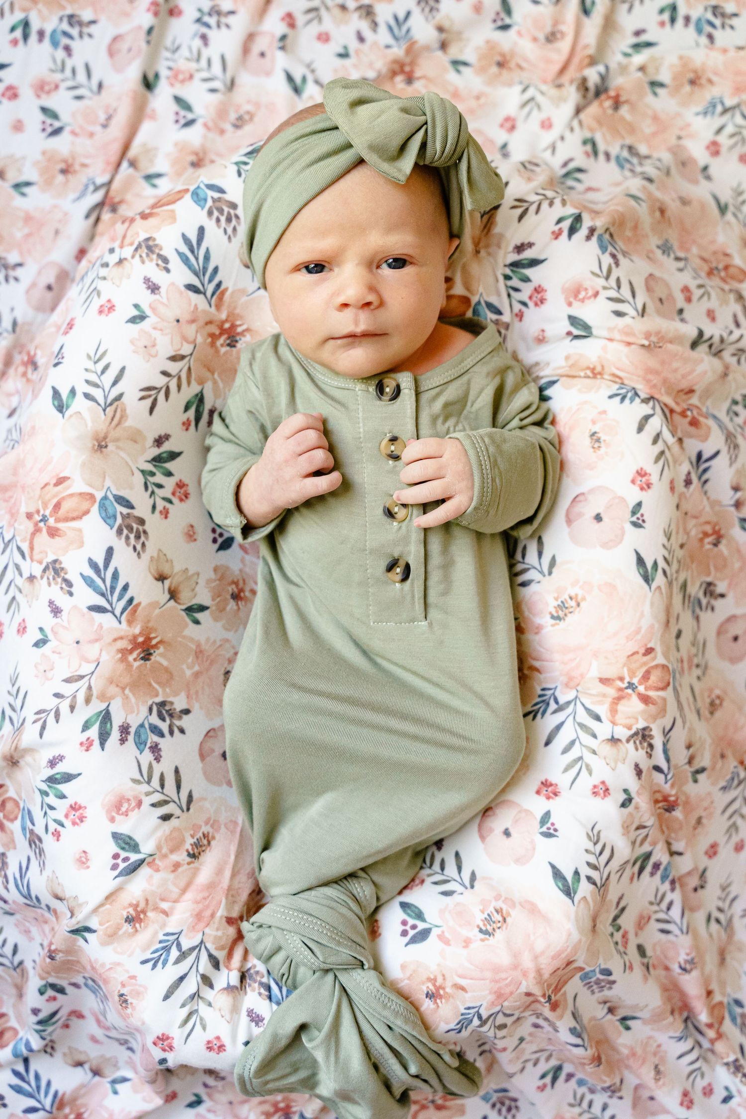 Baby in sage green ribbed outfit lying on floral pattern blanket with matching headband.