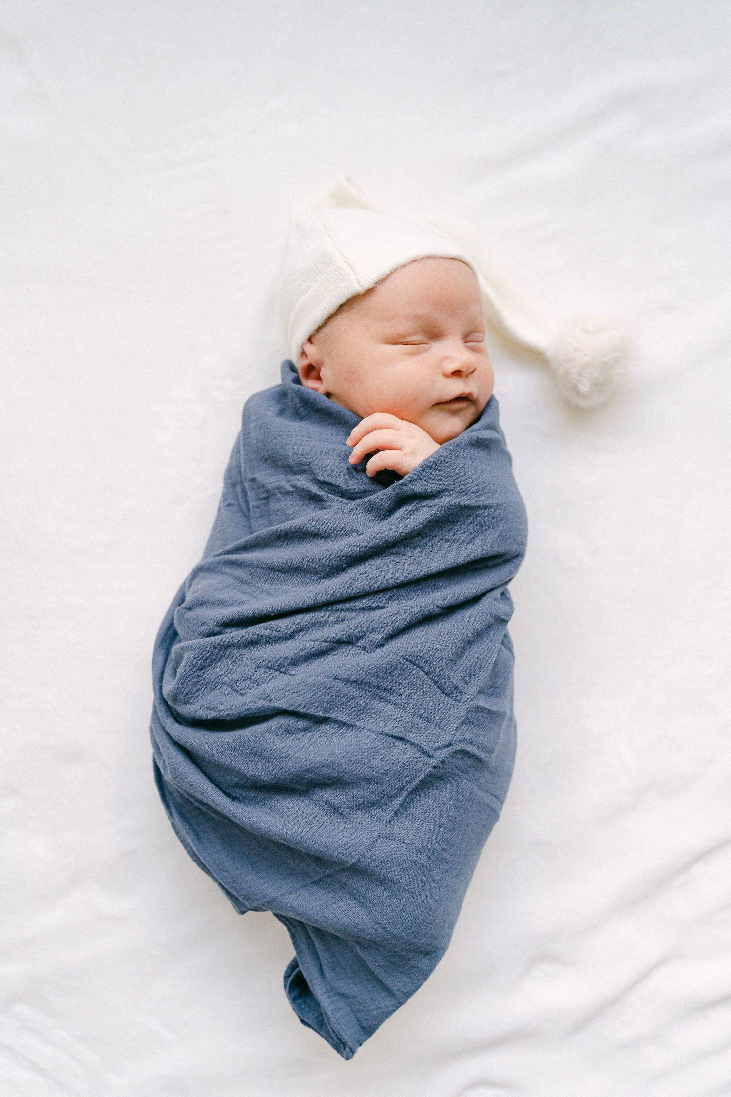 A sleeping newborn baby wrapped in a blue swaddle blanket on white bedding.