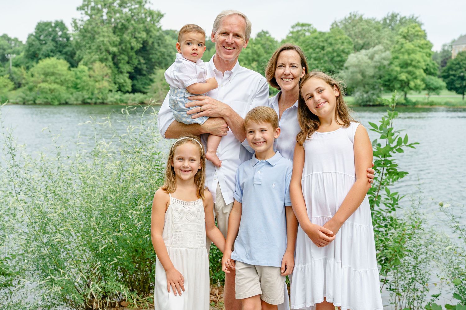 A group in coordinating outfits stands together by a lakeside with lush greenery in the background.