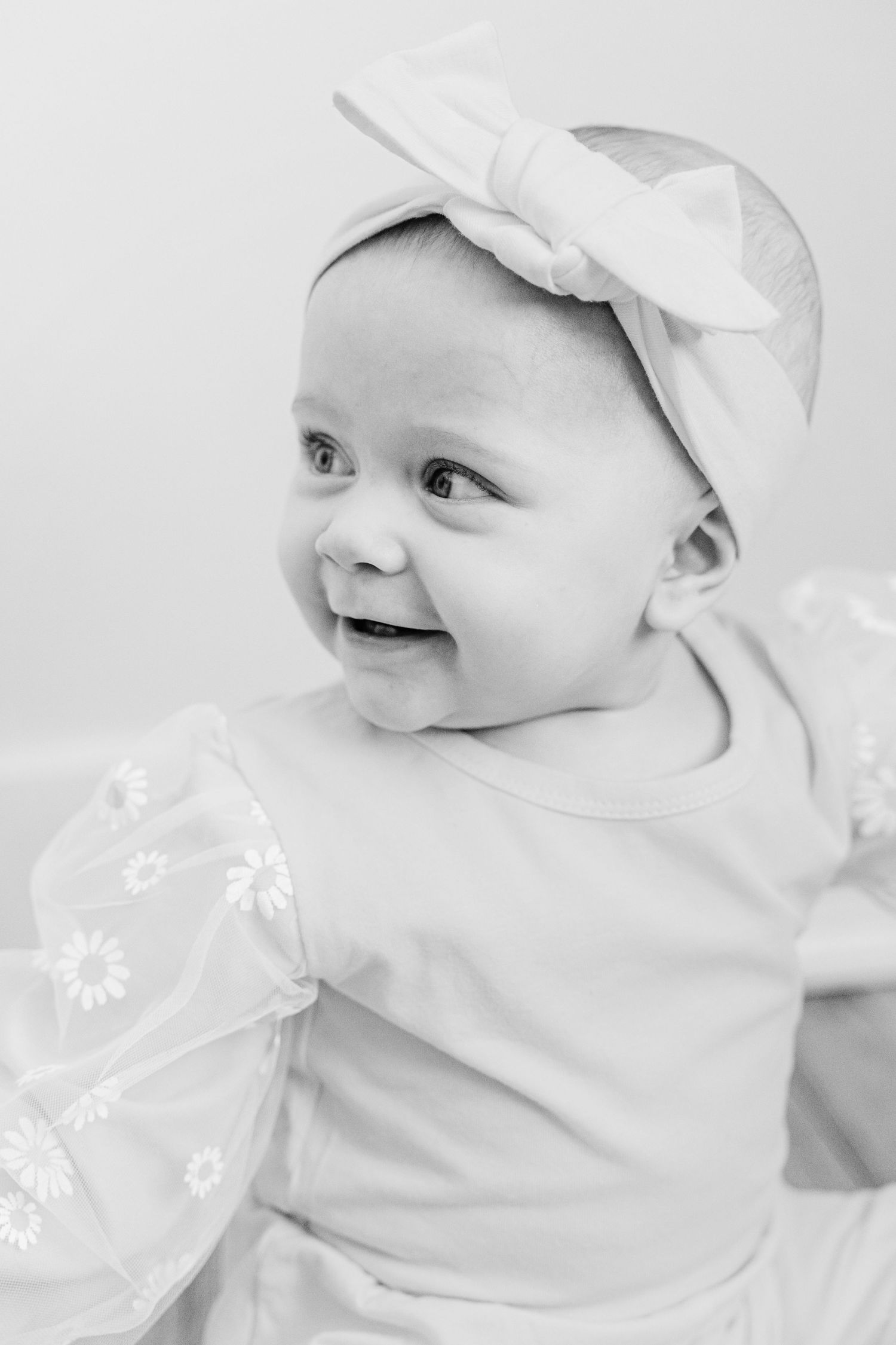 Black and white close-up portraits of a baby wearing a white headband with delicate floral details.