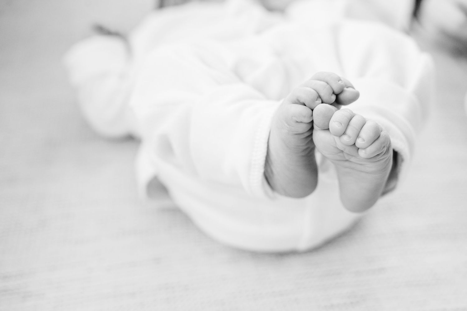 Close-up black and white photo of tiny newborn baby feet wrapped in soft white fabric.