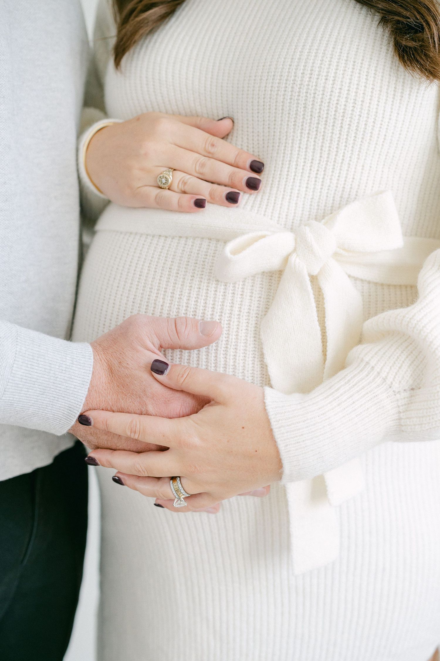 Close-up shots of hands resting on a white knit sweater showing a delicate engagement ring.
