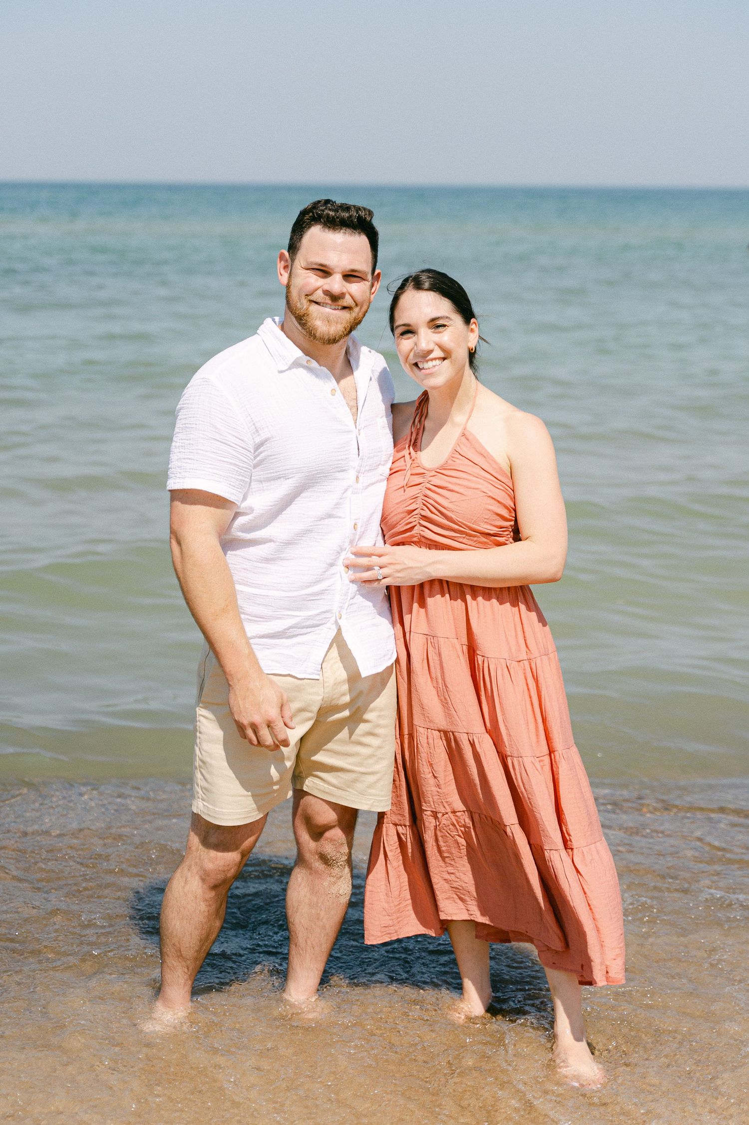 A couple enjoys a romantic moment together at the water's edge on a bright summer day.