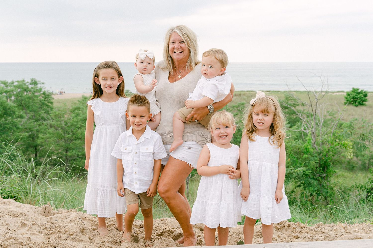 A group in white outfits poses together on a sandy beach during a sunny summer day.