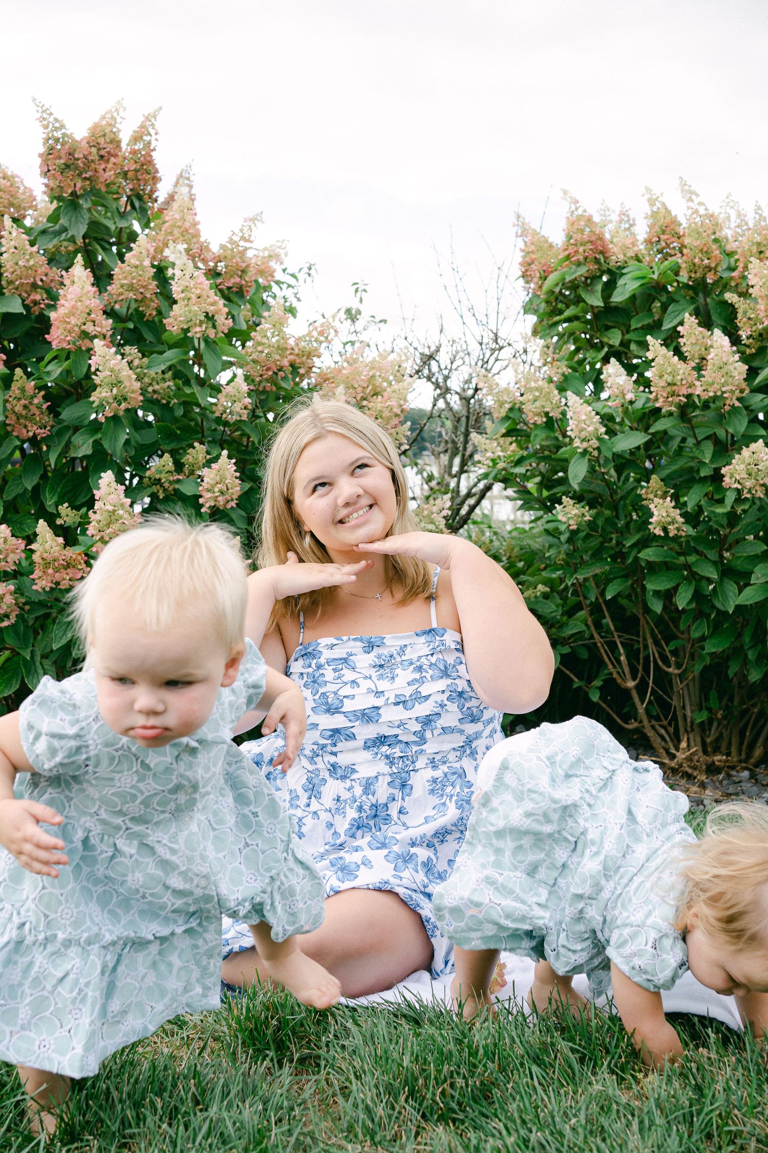 A series of outdoor photos showing a mother and child laying in grass near blooming hydrangea bushes wearing blue and white outfits.