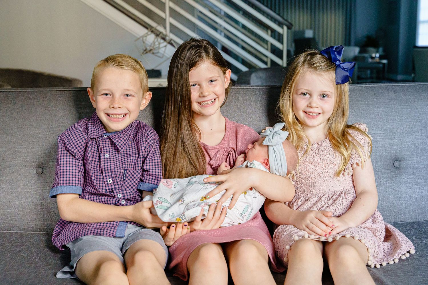 A row of children sitting together on a gray bench wearing coordinated pink and purple outfits.