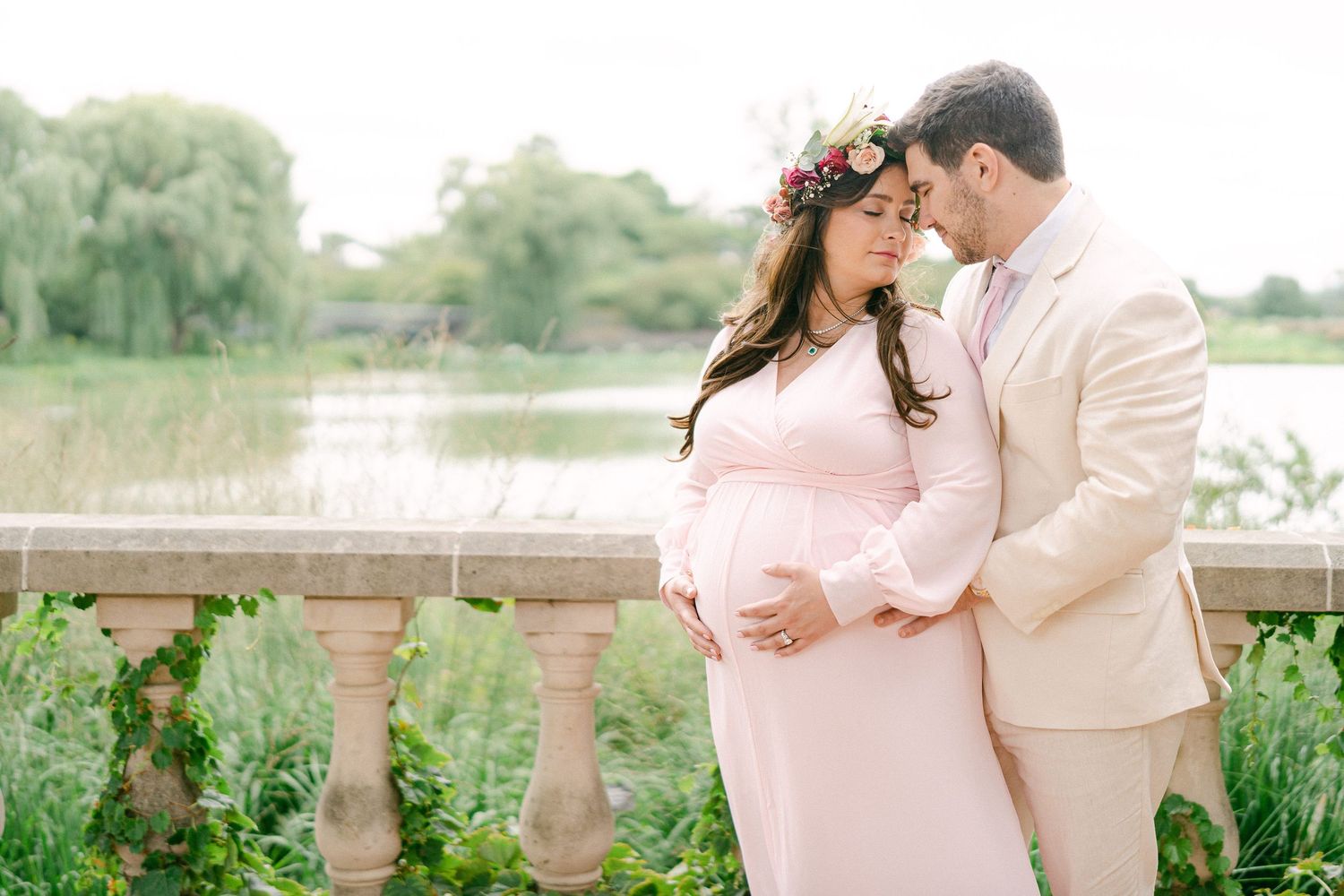A romantic couple in light pink and beige attire embraces during an outdoor photoshoot in a lush garden setting.