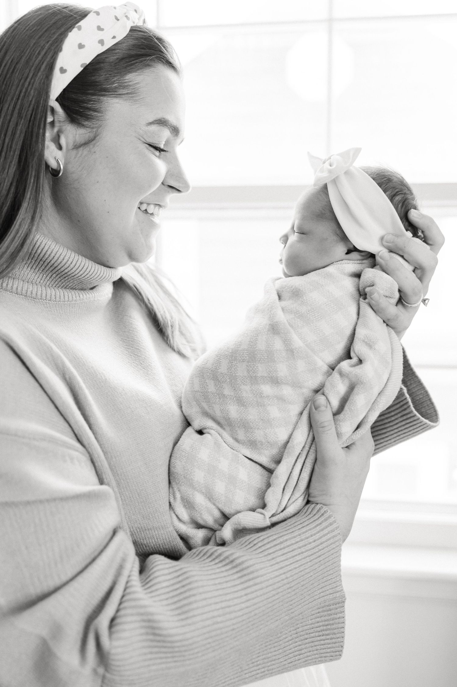 A joyful moment between parent and newborn baby both wearing matching light colored outfits and headbands.
