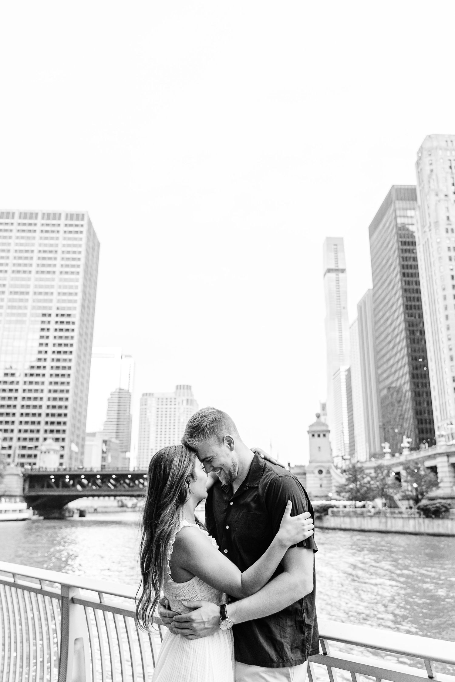 A romantic couple shares intimate moments in a series of black and white photos along a waterfront with city skyline views.