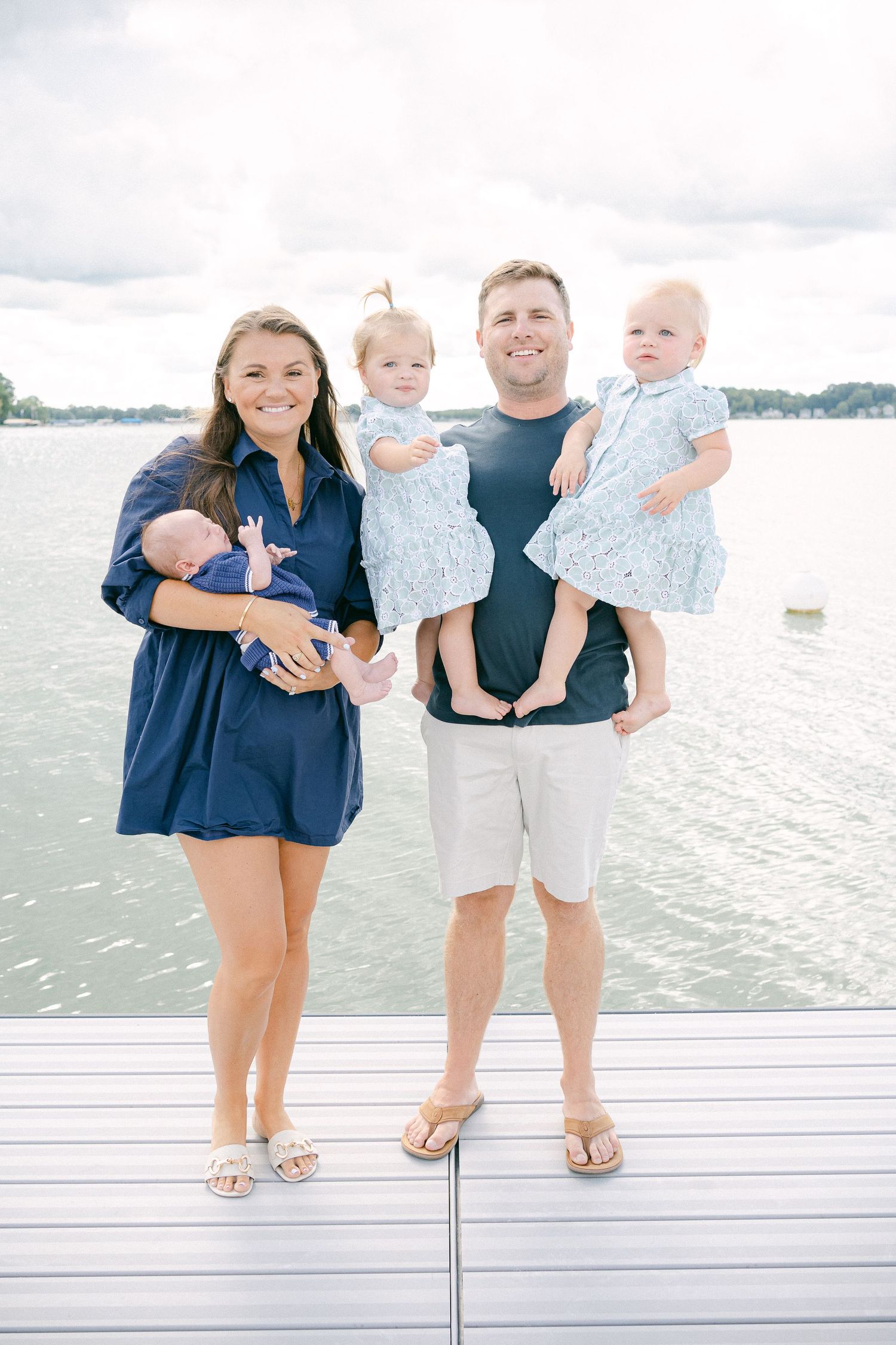 A family stands together on a wooden dock by the water wearing coordinated blue and white summer outfits.