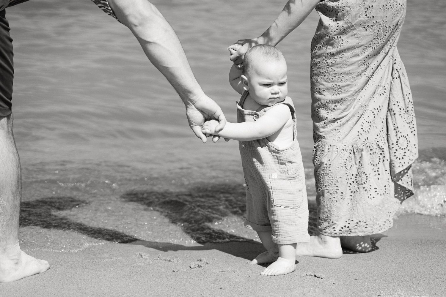 Baby feet walking on sand at the beach with adult guidance.