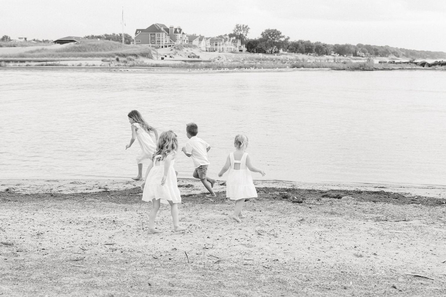 Children in white clothing pose for family photos on a scenic beach with ocean and cliffs in the background.