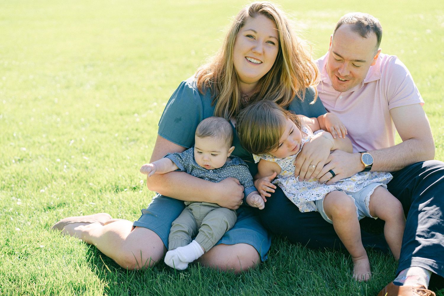 A family sits together on green grass during a sunny outdoor photo session.