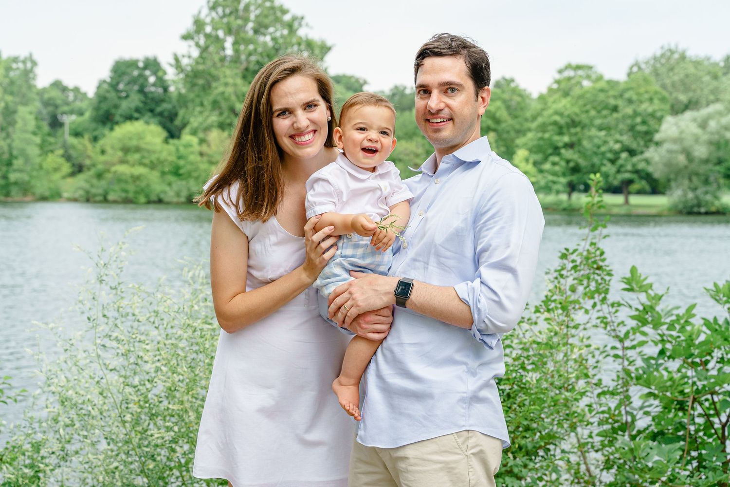 Group portrait taken outdoors with a serene lake and flowering plants in the background.