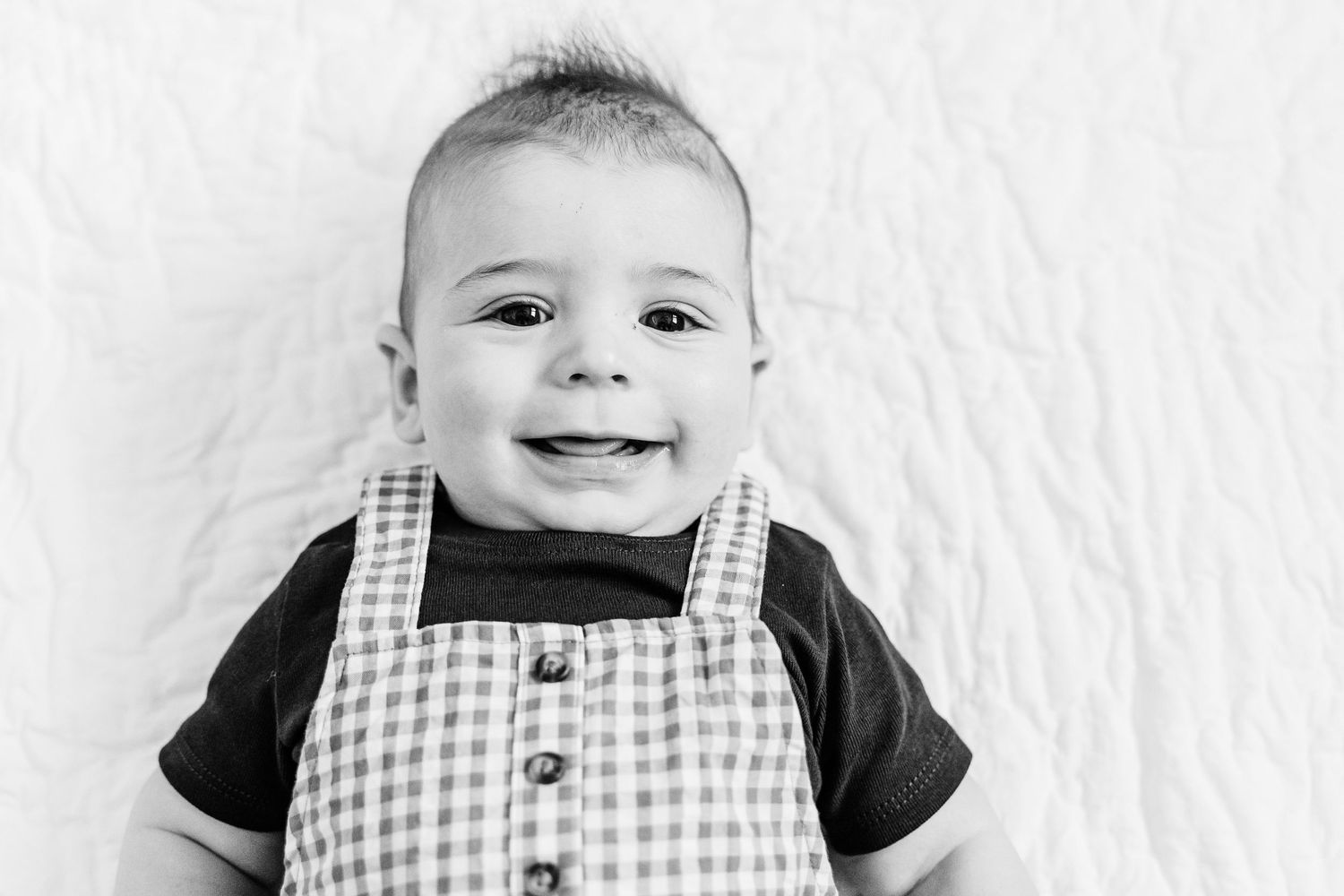 Smiling baby wearing black and white gingham overalls in a series of four progressive photos.