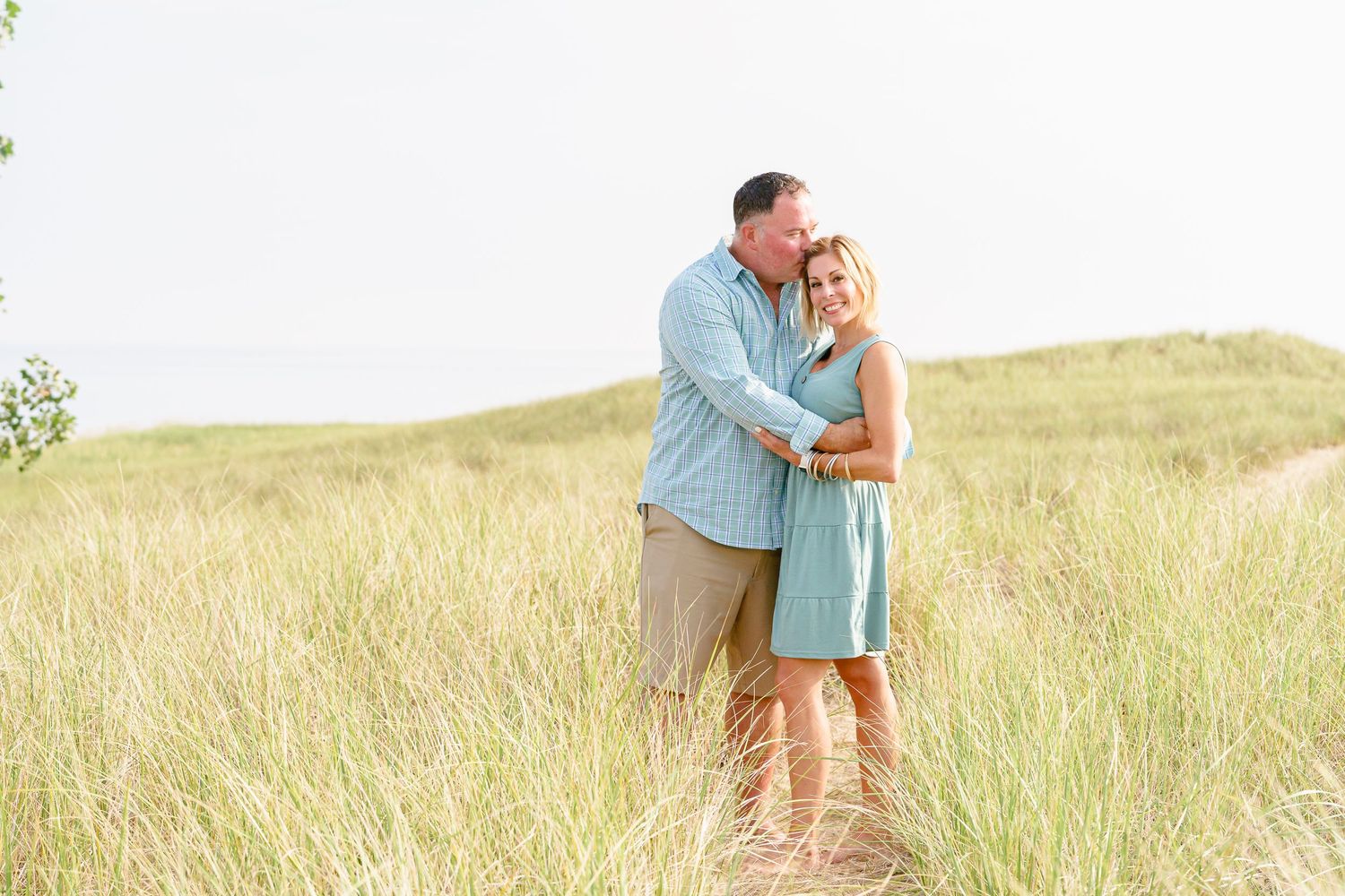 Romantic couple embraces in a sun-drenched field of tall grass during golden hour.