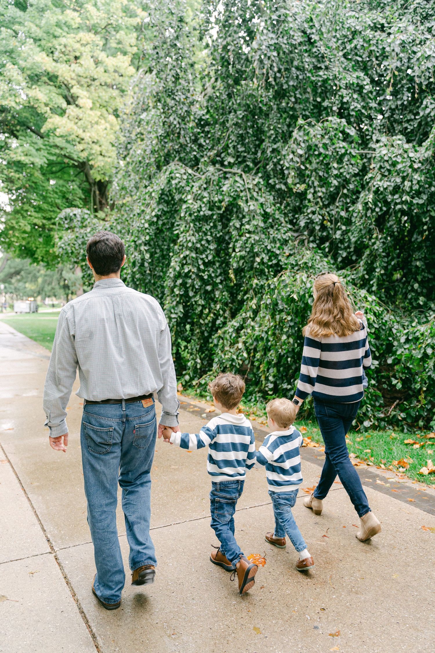 A family walks together on a sidewalk path surrounded by blooming spring trees on a sunny day.