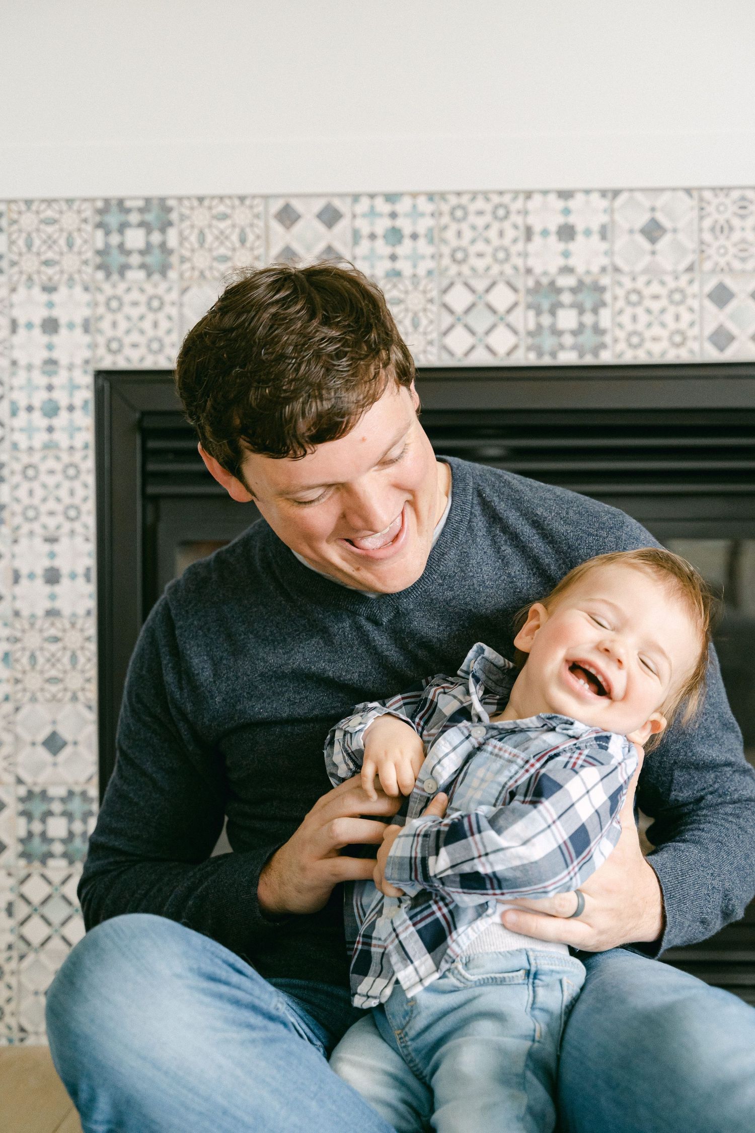 Playful family moment on a couch with patterned tile background showing joyful interaction and laughter.