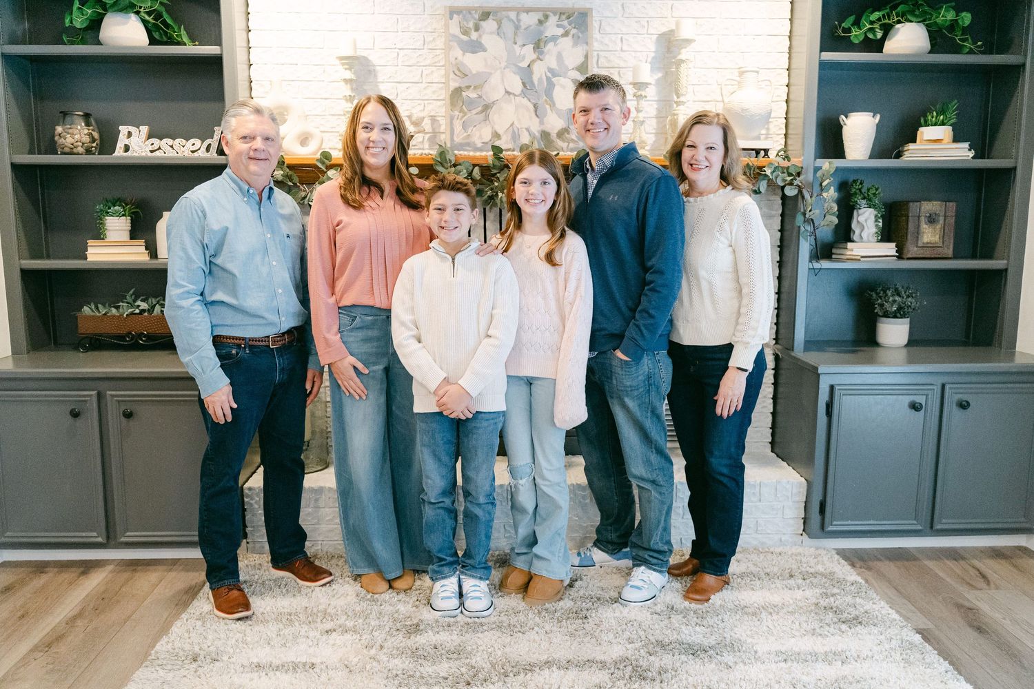 Family gathering in living room with gray built-in cabinets and floral wallpaper backdrop.