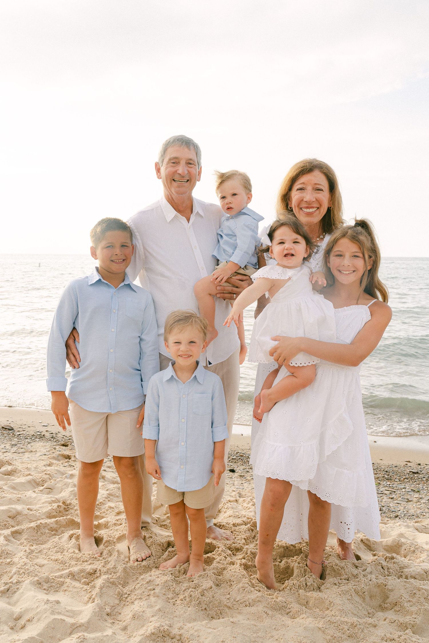 A series of four casual beach family portraits showing a group in coordinated light blue and white outfits on sandy shore.