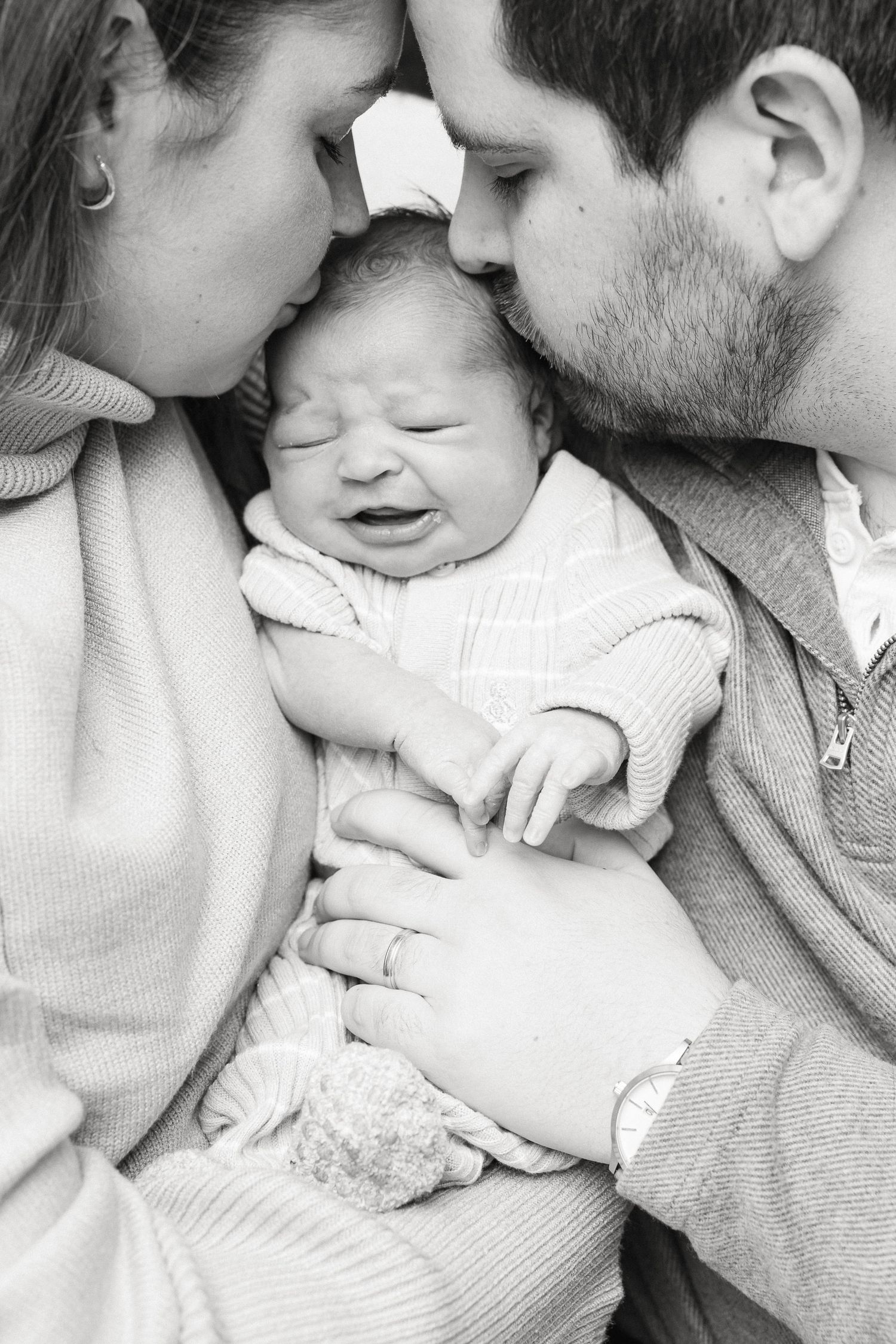 Black and white intimate portrait of parents tenderly embracing their newborn baby.
