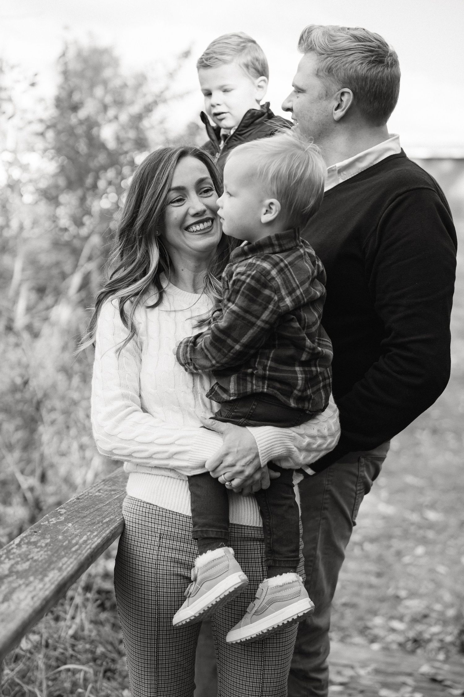 Family shares joyful candid moments together during an outdoor autumn photoshoot in black and white.