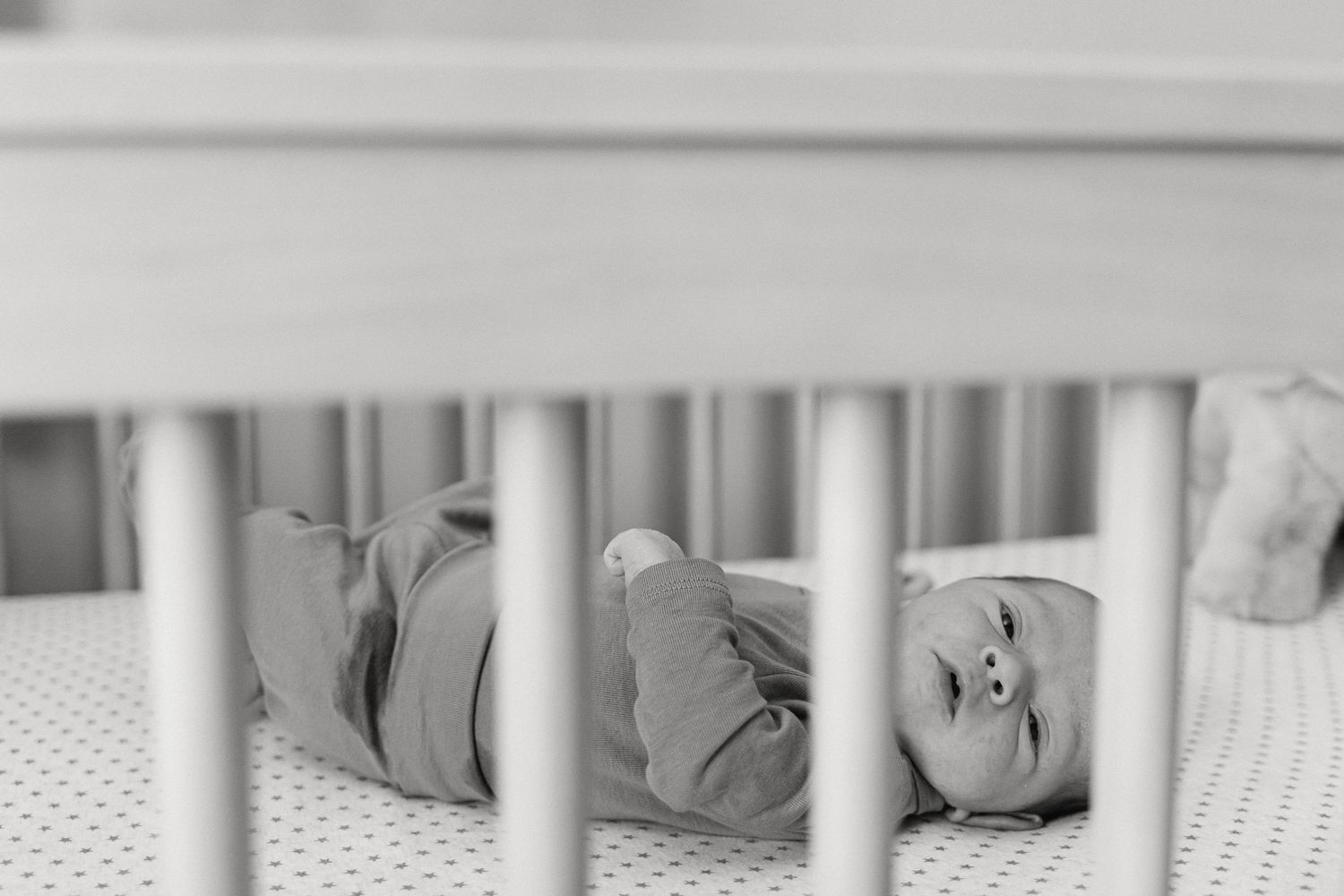 Close-up view of white crib bedding with delicate pattern details in a minimalist nursery setting.