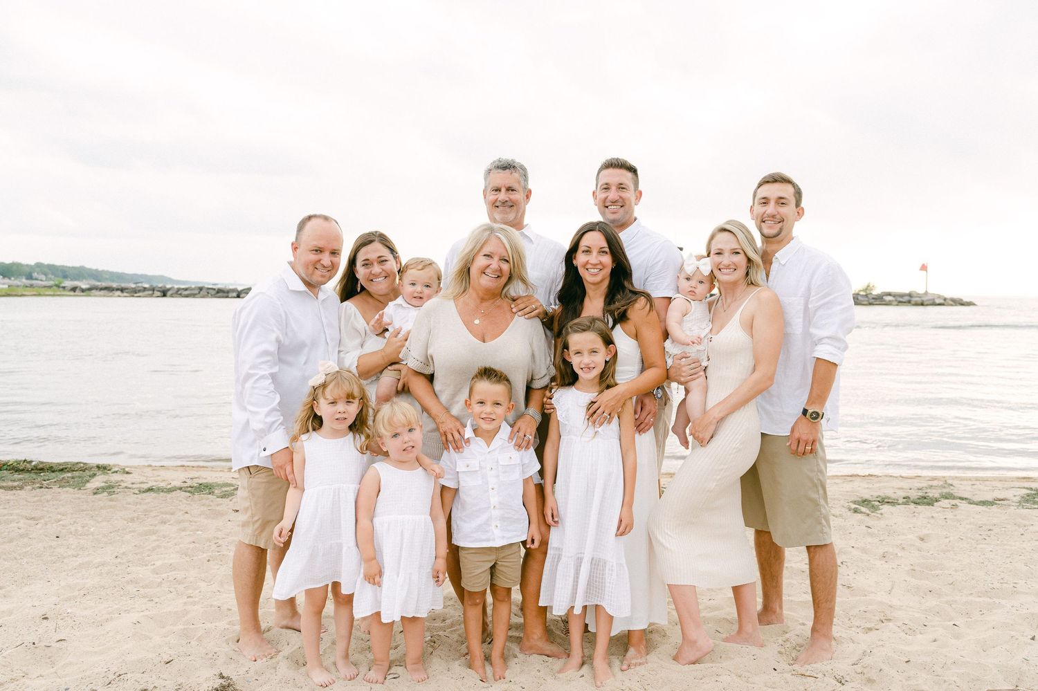 A group wearing coordinated white outfits poses together on a sunny beach at sunset.