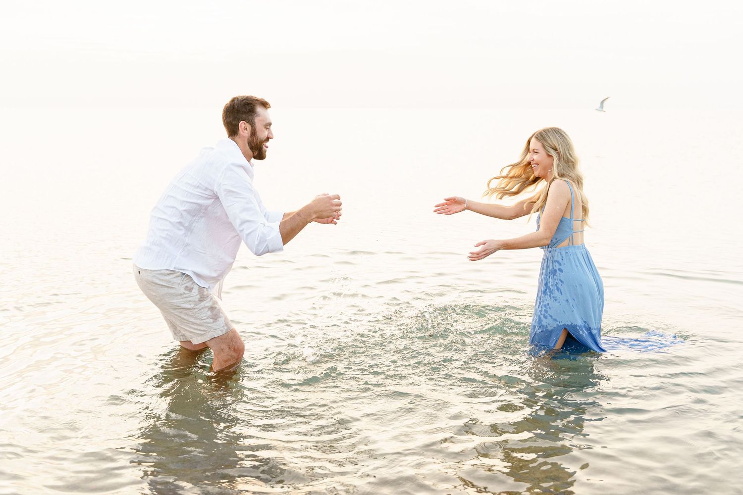 A couple splashes and plays together in the shallow ocean water during a bright sunny day at the beach.