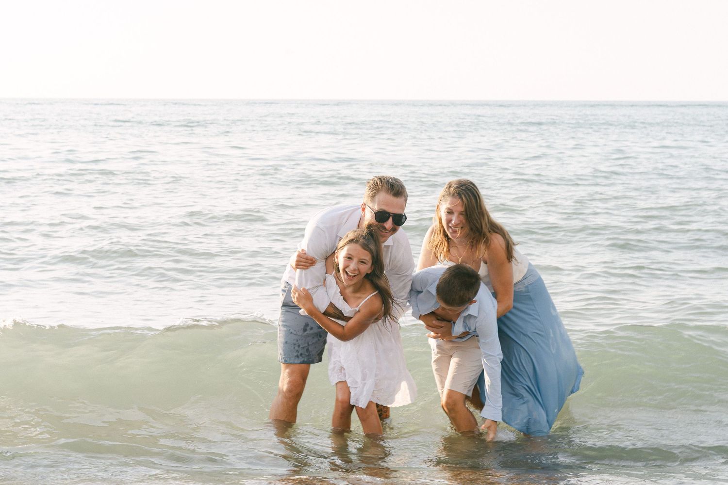 A family enjoys a playful moment together in the ocean waves on a bright sunny day at the beach.